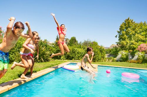 Group of happy friends, teenage boys and girls, jumping in outdoor swimming pool in summer